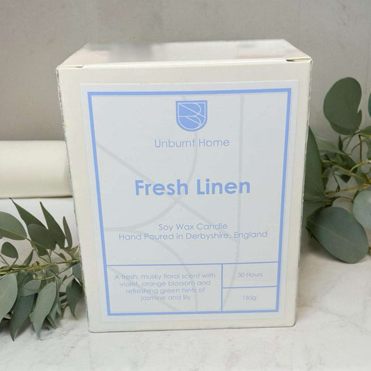 Fresh Linen Candle on white stone surface with fresh linen and leaves in the background