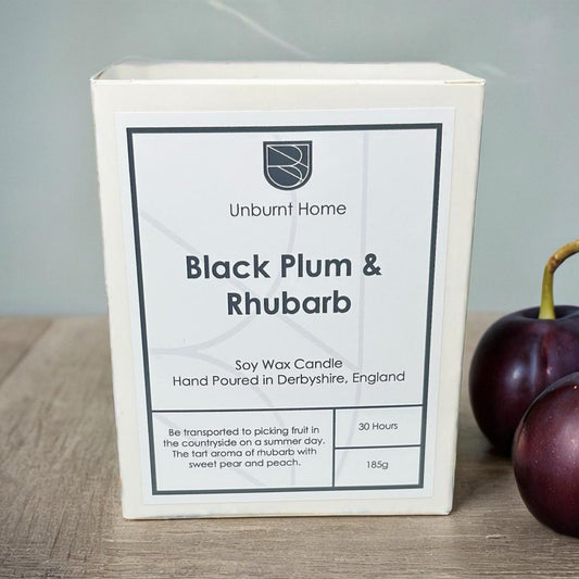 Plum candle in box on hard wood surface with plums in the background