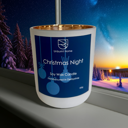 Christmas night candle on a window sill in front of a window.  Outside is a distant winter scene with stars in the sky.