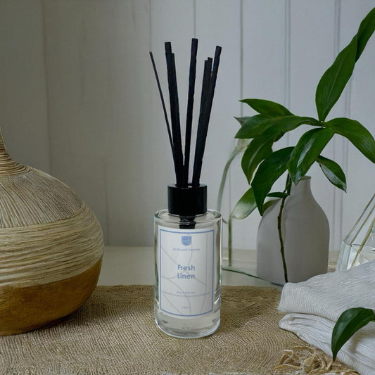 Fresh Linen Reed Diffuser on rattan surface with vases and leaves in the background