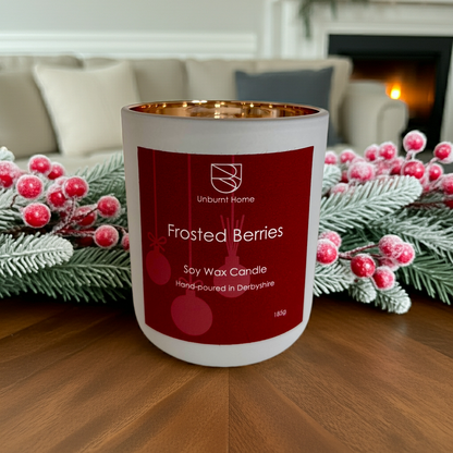 Frosted berries Christmas candle on a wooden table in a living room surrounded by a frosted berry and pine garland