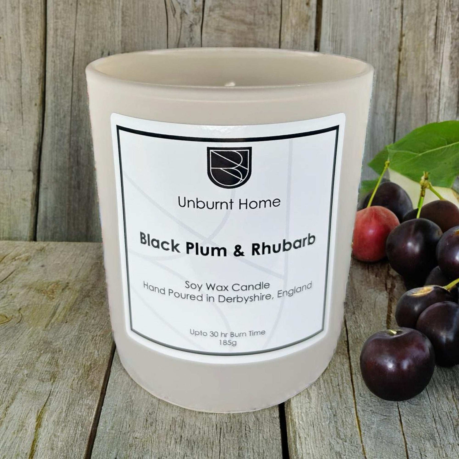 Rhubarb candle on hard wooden surface with plums in the background